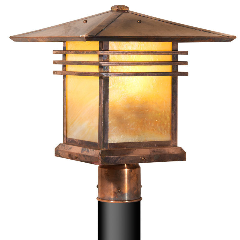 Copper outdoor post light with a warm glow on a white background