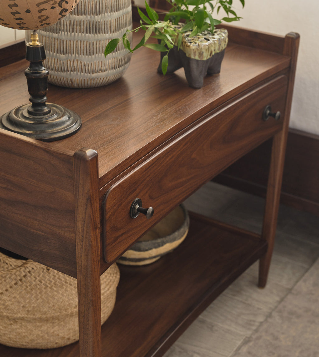 Wooden side table with a lamp, plants, and woven baskets on top.