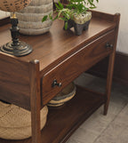Wooden side table with a lamp, plants, and woven baskets on top.