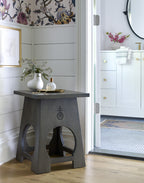 Table with a decorative design in a room with floral wallpaper and white cabinets.