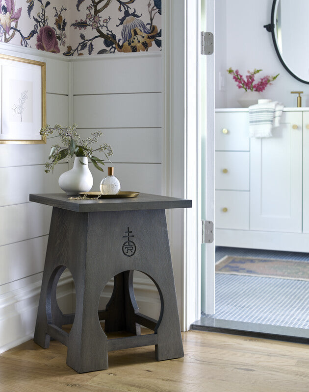 Table with a decorative design in a room with floral wallpaper and white cabinets.