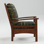 A mid-century modern wooden armchair with dark green and navy floral patterned cushions, shown from a three-quarter angle against a light gray studio background.