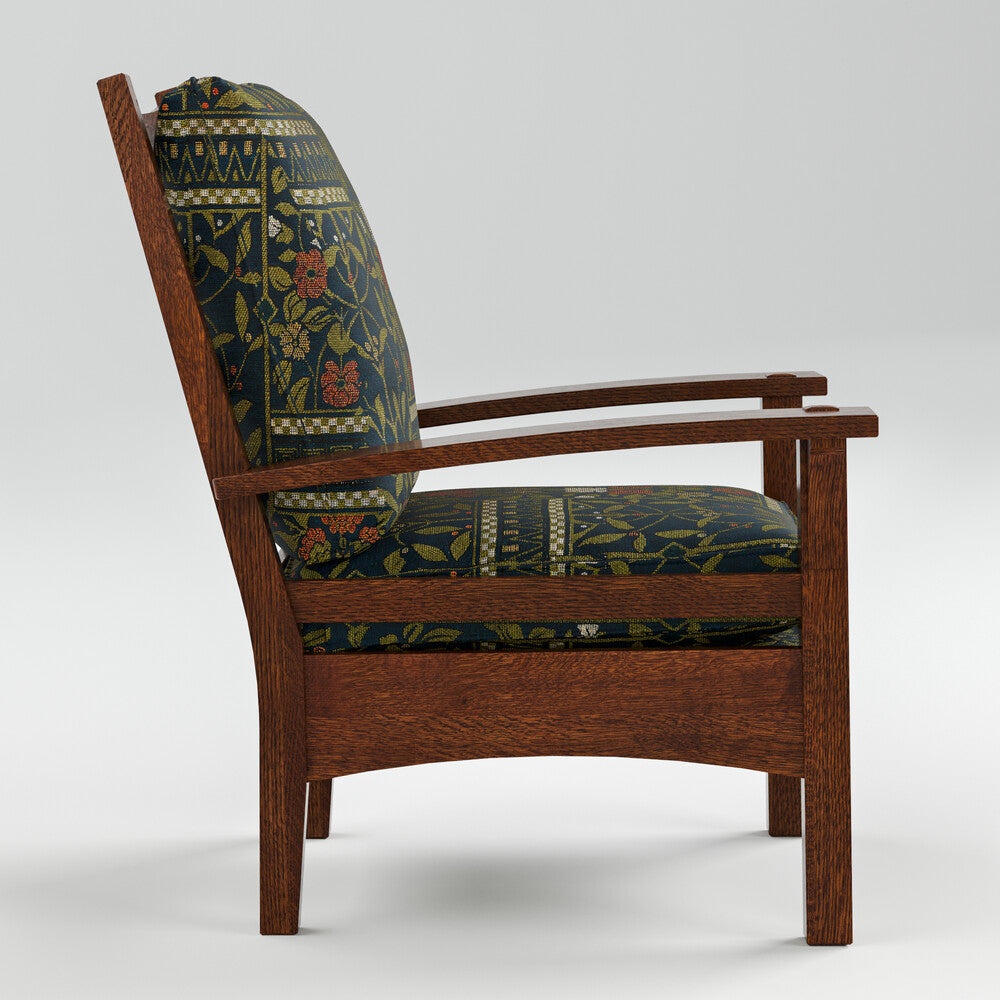 A mid-century modern wooden armchair with dark green and navy floral patterned cushions, shown from a three-quarter angle against a light gray studio background.