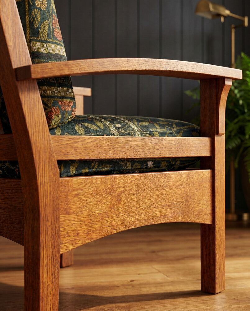 A close-up of a wooden armchair with a warm medium-brown oak frame and patterned green, blue, and red cushions, set in a room with dark paneled walls and a wooden floor.