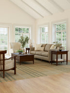 Living room with beige sofa, wooden coffee table, and armchair in a bright room with large windows.
