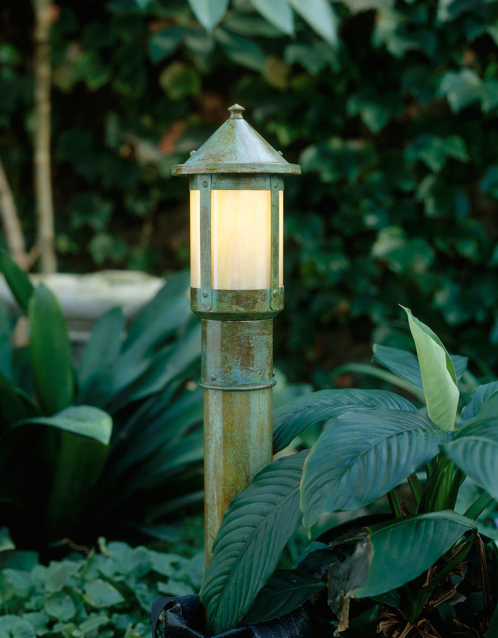 Garden lamp post with a warm glow surrounded by green foliage