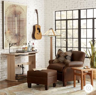 Living room with brown sofa, ottoman, and coffee table in front of a brick wall.