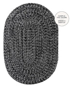 An oval braided area rug in a black and white heathered pattern, shown from a top-down view on a white background with a circular text overlay in the top right that reads 'SAMPLE THE COLORS ORDER A SWATCH'.