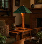 A rustic wooden table lamp with a green textured conical shade and a warm-toned wooden base, styled on a wooden side table in a cozy, dimly lit living room.