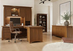 A warm brown wooden home office furniture set including a desk, hutch, chair, bookcase, and sideboard, arranged in a modern room with light wood floors and white walls.