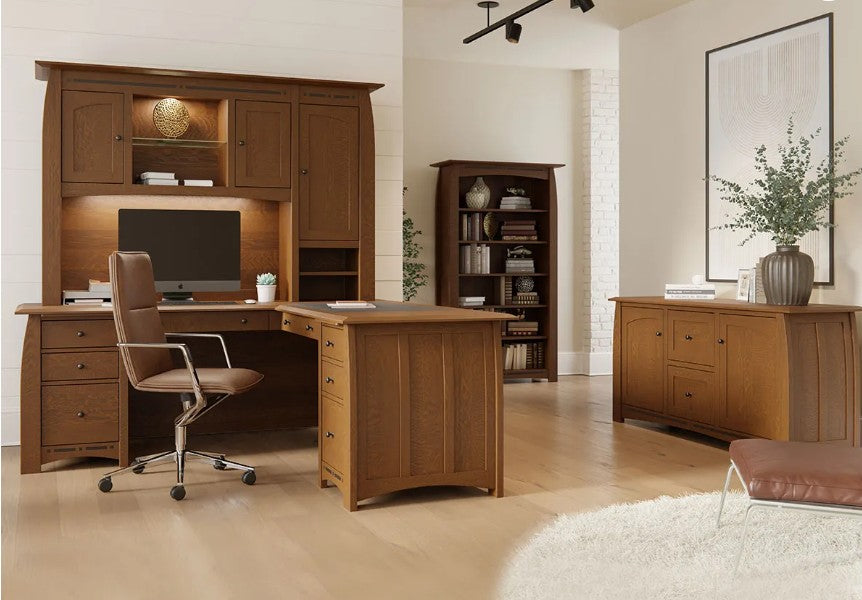 A warm brown wooden home office furniture set including a desk, hutch, chair, bookcase, and sideboard, arranged in a modern room with light wood floors and white walls.