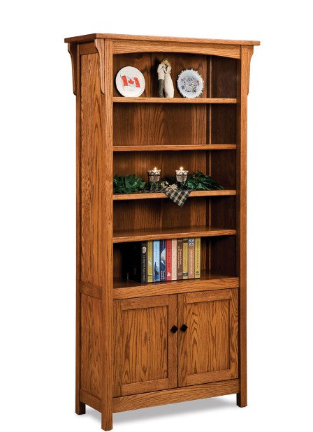 A tall wooden bookcase with a warm medium-brown finish, featuring five open shelves, decorative items on the top shelf, a green garland and candle holder on the middle shelves, and two cabinet doors at the bottom. The bookcase is shown against a plain white background.