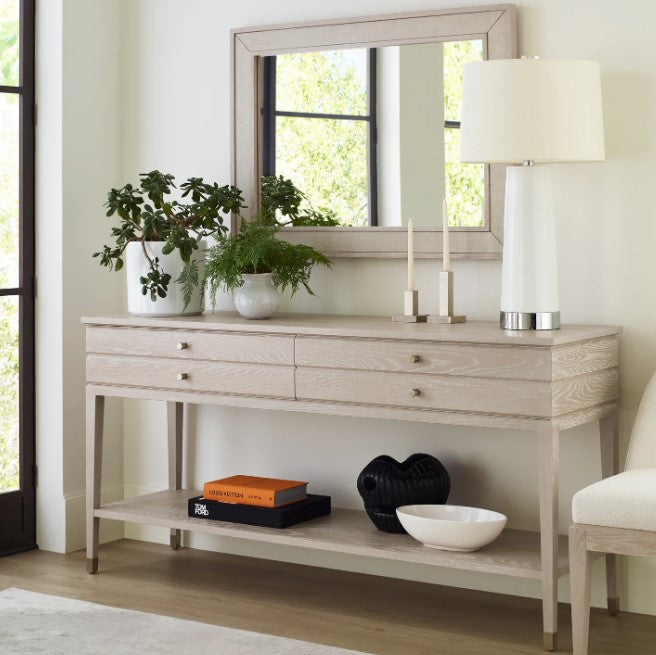 Light wood console table with decorative items in a room with a mirror and lamp.