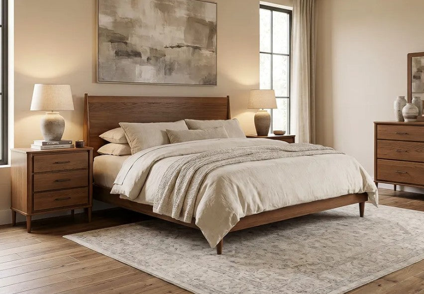 A mid-century modern wooden bed frame with a matching headboard and footboard, styled in a warm beige bedroom with two matching nightstands, lamps, a dresser, and a large abstract painting.