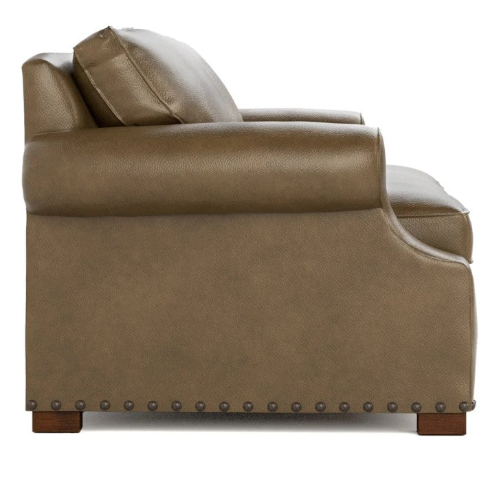 Side view of a brown leather armchair with nailhead trim and dark wooden legs, shown against a plain white background.