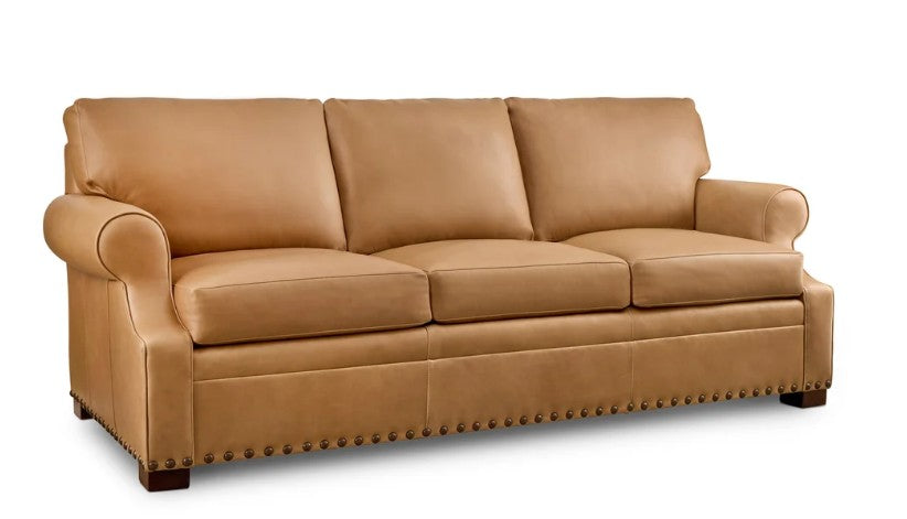 A tan leather three-seater sofa with rolled arms, deep seat cushions, and nailhead trim along the base, shown on a plain white background.