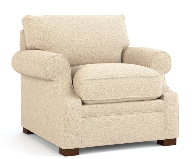 A classic upholstered armchair in a textured cream-beige fabric, featuring rolled arms, a high back cushion, and dark brown wooden legs, shown against a plain white background.