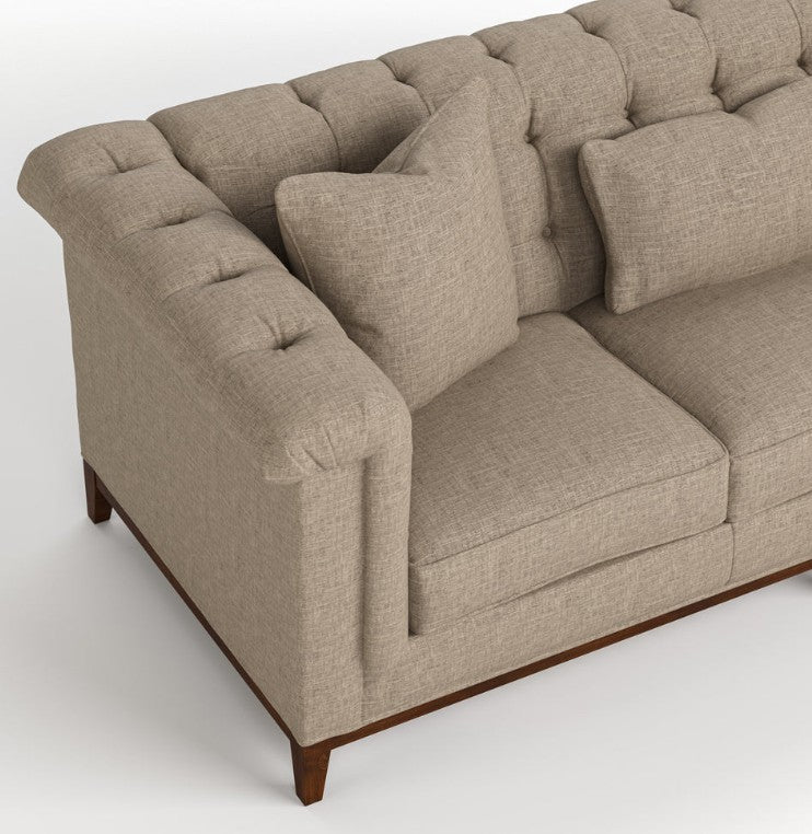 A close-up of a tufted loveseat sofa upholstered in a textured beige fabric, featuring dark brown wooden legs, shown against a light gray background.