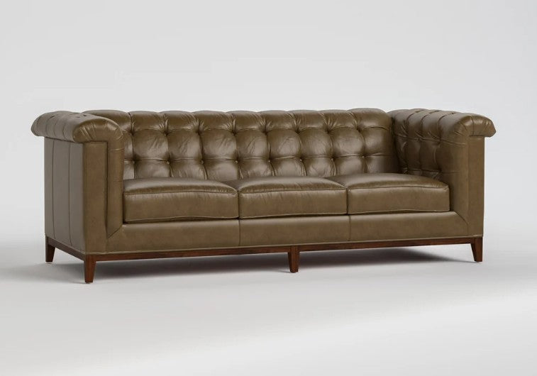 A classic Chesterfield-style leather sofa in a warm taupe-brown color, featuring deep button tufting, rolled arms, and dark wood legs, shown against a neutral light gray background.