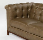 A close-up of a brown tufted leather sofa showing the backrest, armrest, seat cushion, and a portion of the wooden leg against a plain white background.