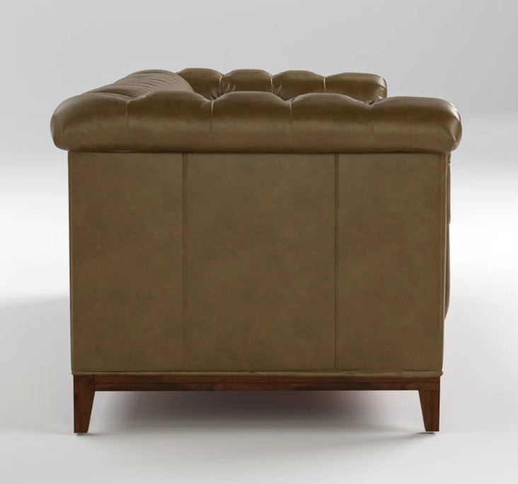 A brown leather Chesterfield sofa shown from the rear three-quarter view, featuring deep button tufting on the backrest and a dark wood base with tapered legs, set against a neutral light gray studio background.