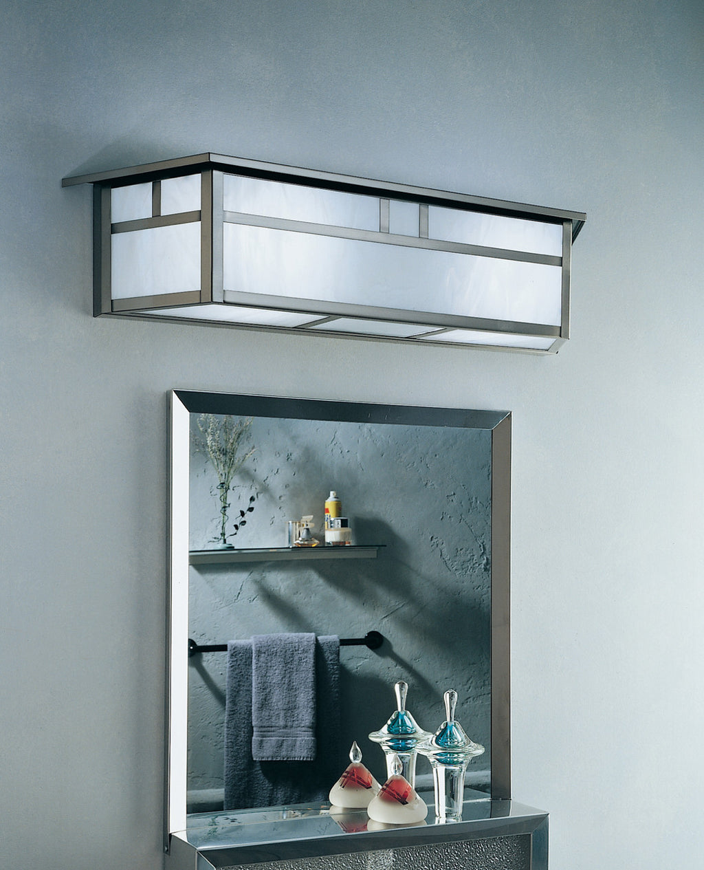 Ceiling light fixture above a mirror with decorative items on a gray wall.