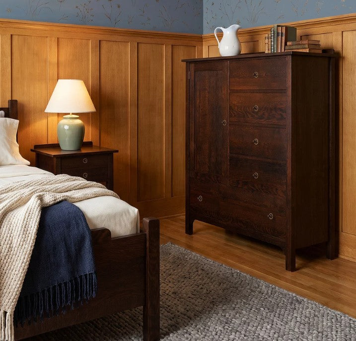 A dark brown wooden dresser with five drawers and small round knobs, shown in a styled bedroom next to a bed and nightstand.
