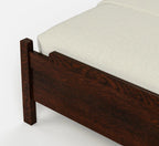 Close-up of a dark brown wooden bed frame corner with a light beige textured mattress or bedding on a clean white background.