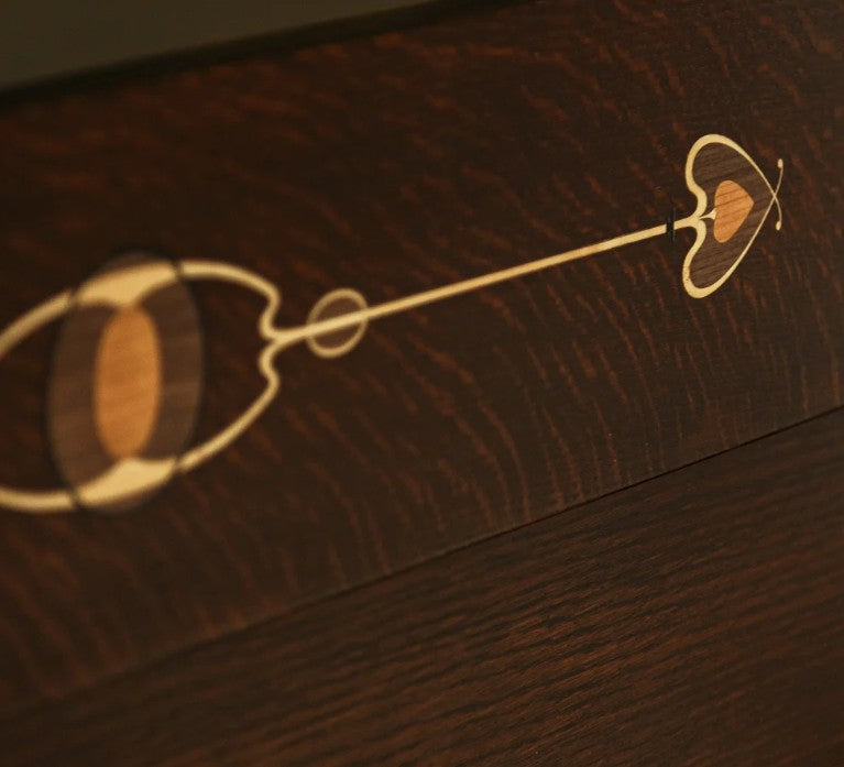 Close-up of a dark brown wooden surface with a decorative light wood inlay featuring a heart, oval, and line motif.
