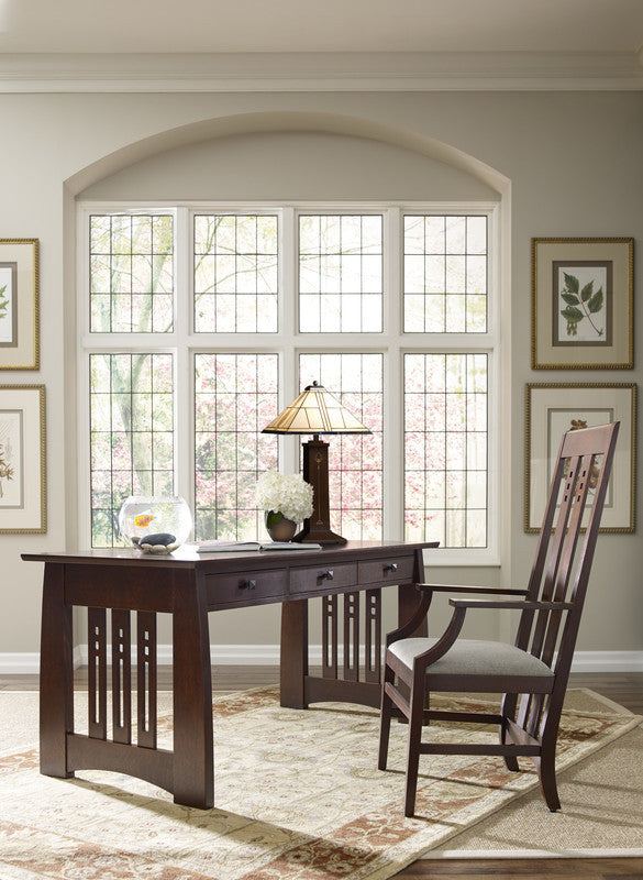 Wooden desk with chair in a room with large windows and framed pictures on the wall.