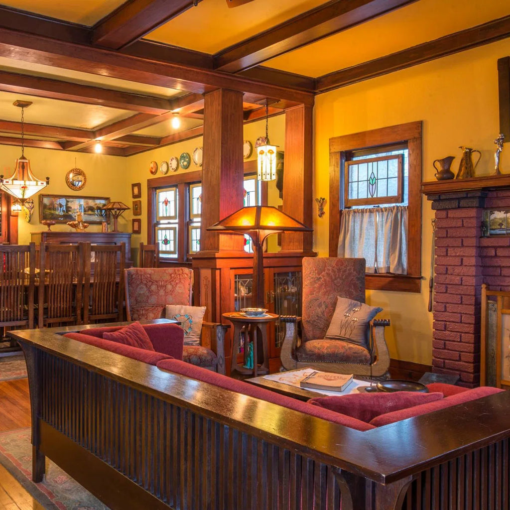A warm, traditional interior room with wood ceiling beams, yellow walls, a brick fireplace, and a large wooden sofa with red cushions in the foreground.
