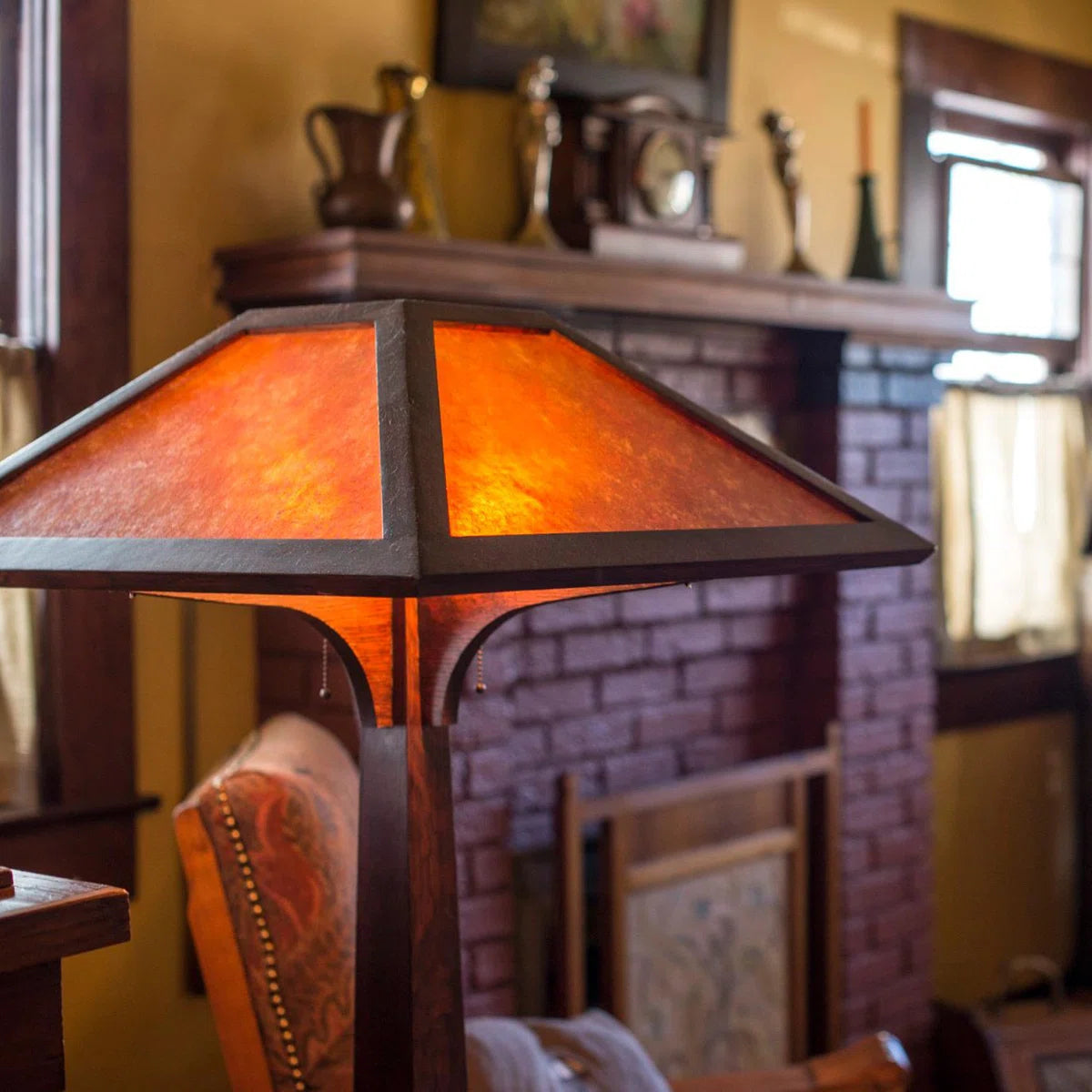 A vintage-style table lamp with a dark wood frame and textured orange glass panels, lit and placed in a cozy room in front of a brick fireplace.