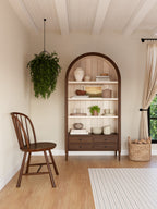Wooden bookshelf with decorative items in a room with a chair, rug, and plants.