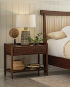 Wooden nightstand with decorative items next to a bed in a bedroom setting