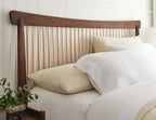 Bed with wooden headboard, white bedding, and beige pillows against a white wall.