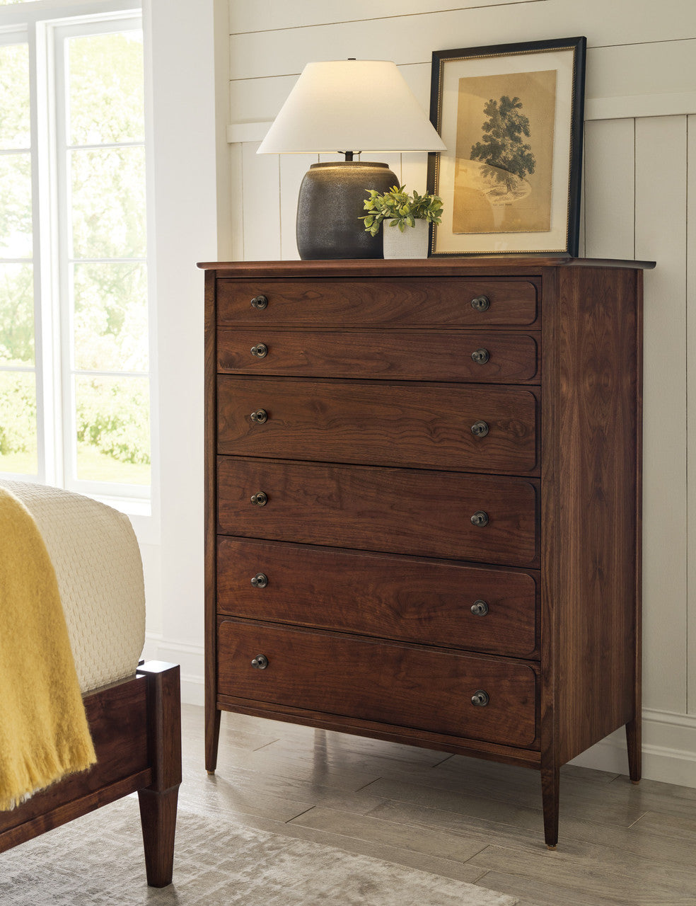 Wooden dresser with decorative items in a room with a bed and window.