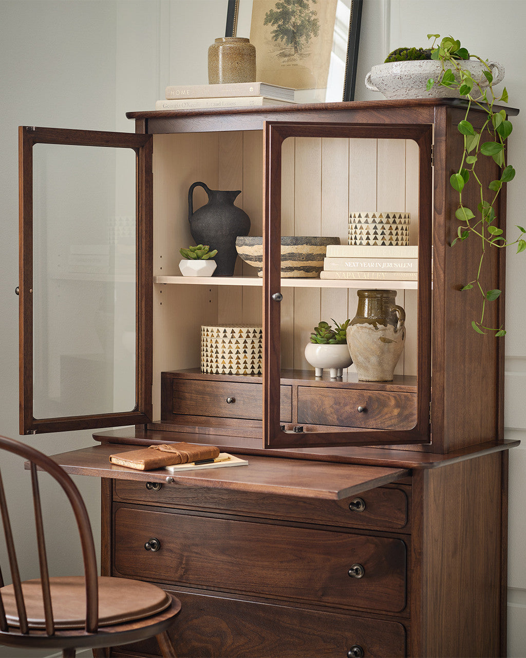 Wooden cabinet with open doors displaying decorative items, accompanied by a chair.
