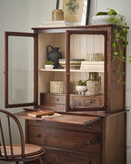 Wooden cabinet with open doors displaying decorative items, accompanied by a chair.