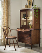 Wooden desk with glass cabinet and chair in a room with curtains and decor.