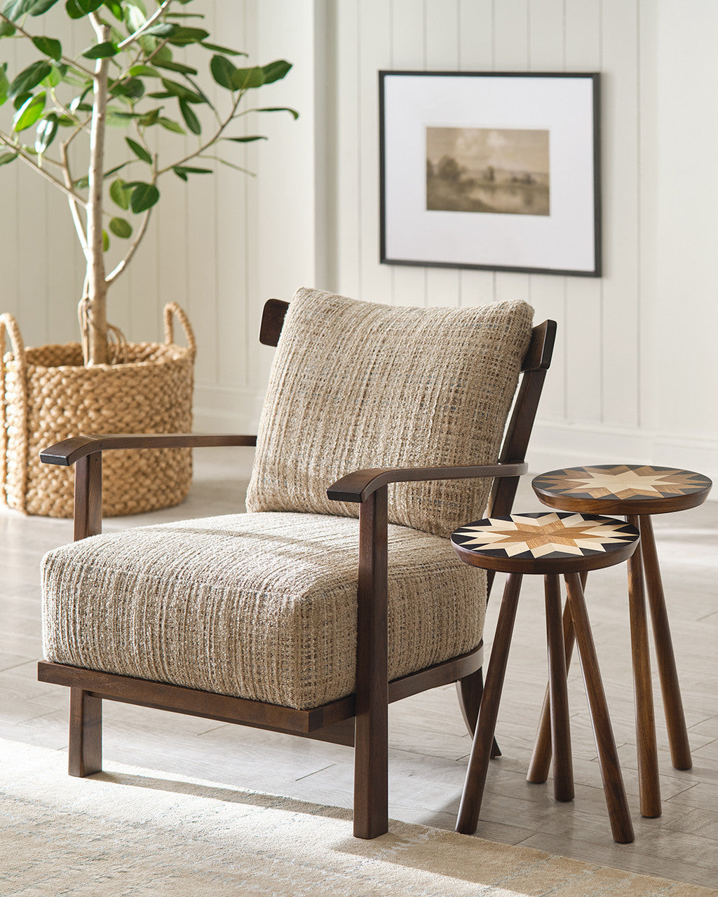 Beige armchair with wooden frame in a room with two small side tables and a plant.