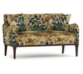 A small upholstered loveseat with rolled arms, dark wood legs, and a dense floral tapestry-style pattern in beige, olive green, and purple on a white studio background.