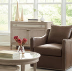 Brown leather armchair in a living room with a round glass coffee table and a cabinet.