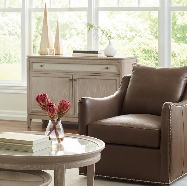 Brown leather armchair in a living room with a round glass coffee table and a cabinet.