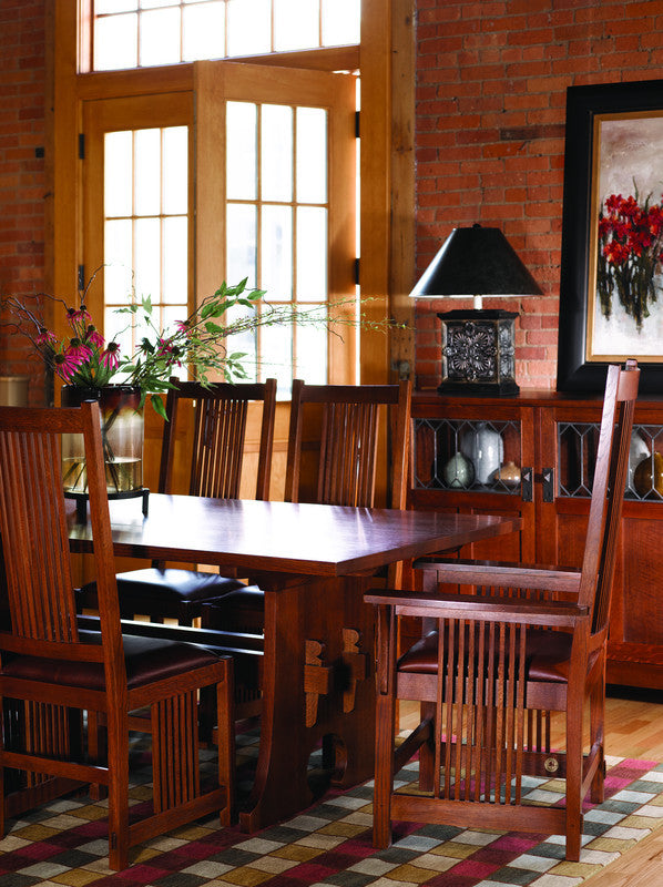 Wooden dining table with chairs in a room with brick walls and large windows.