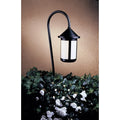Black outdoor lamp post with white flowers and greenery on a beige wall background