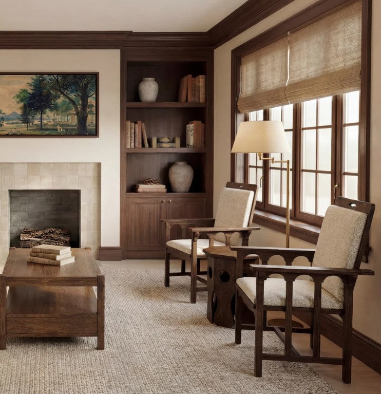A styled living room interior featuring dark wood furniture, including two armchairs with light beige upholstered seats, a matching wooden coffee table, a floor lamp, built-in shelving, and a fireplace.