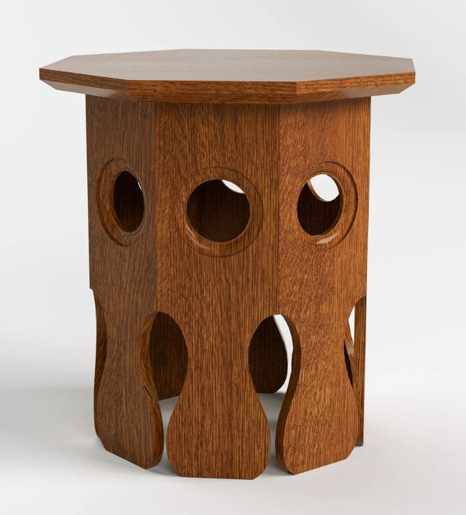 A hexagonal wooden side table with a warm medium-brown finish, featuring a solid octagonal top and a sculptural base with circular and teardrop-shaped cutouts, shown on a light gray background.
