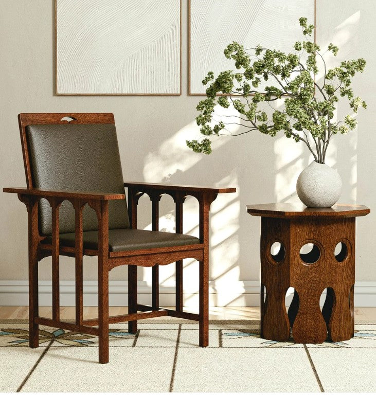 A mid-century modern wooden armchair with dark gray upholstered seat and backrest, positioned next to a matching wooden side table with a white ceramic vase of green branches, set against a neutral beige wall with framed art.
