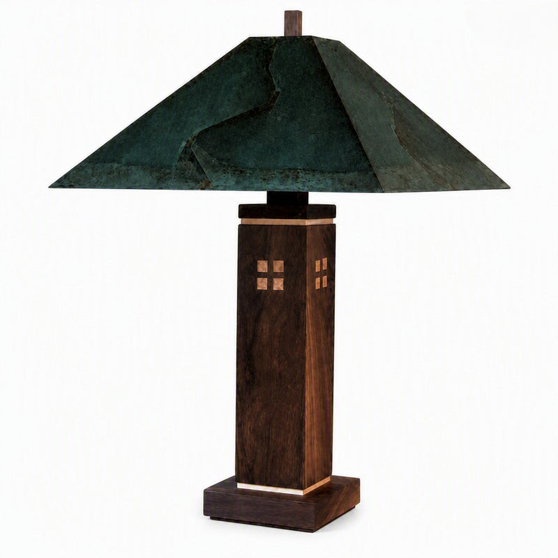 A table lamp with a dark green textured metal pyramid shade and a dark brown wooden pedestal base featuring small geometric inlay details, shown against a plain white background.