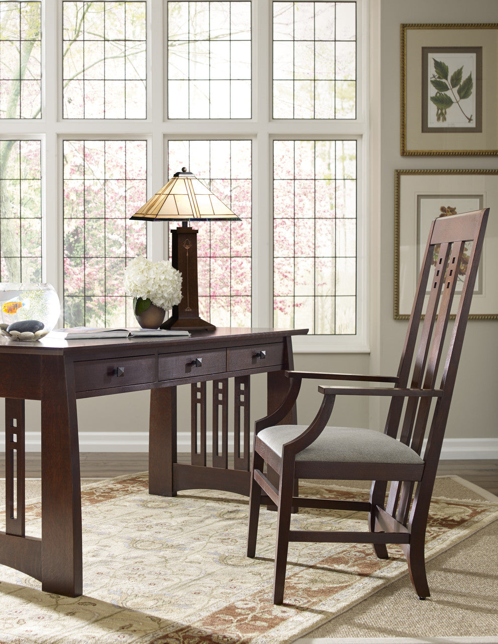Wooden desk with chair in a room with large windows and decorative elements.